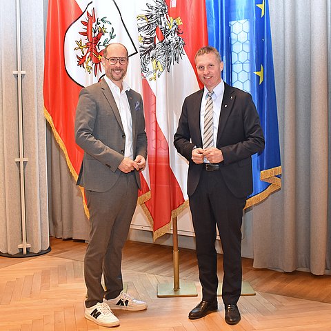 LR Gerber und LR Walcher zusammen vor einer Österreich-, einer Tirol- und einer EU-Flagge.