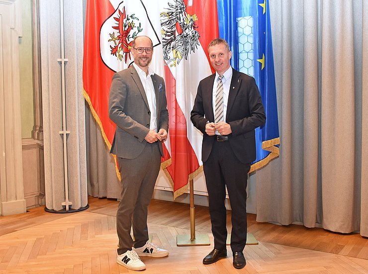 LR Gerber und LR Walcher zusammen vor einer Österreich-, einer Tirol- und einer EU-Flagge.